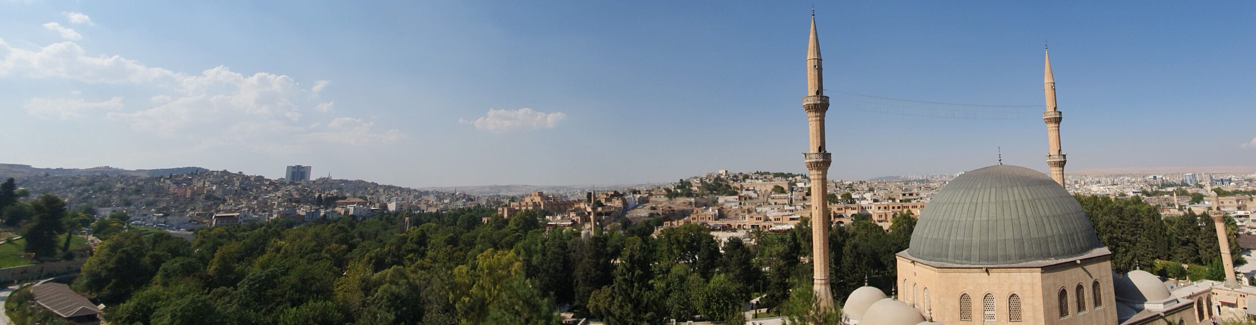 Riha Urfa, Kurdistan – Panorama Panorama of the ancient city of Riha/Urfa. Mosque with large dome and two minarets in foreground. Minaret of the 12th century Halil ul-Rahman Mosque is visible. City gardens. Old honey-colored buildings in the background.